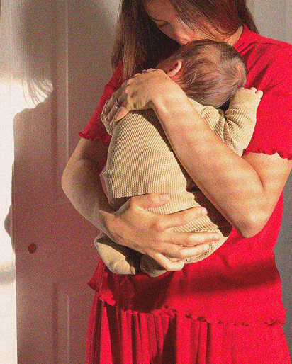 Woman in red dress holding baby dressed in beige ribbed outfit with long sleeves.