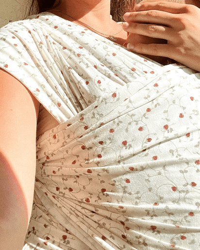 White fabric baby wrap with small red and green floral pattern worn by a person in sunlight.