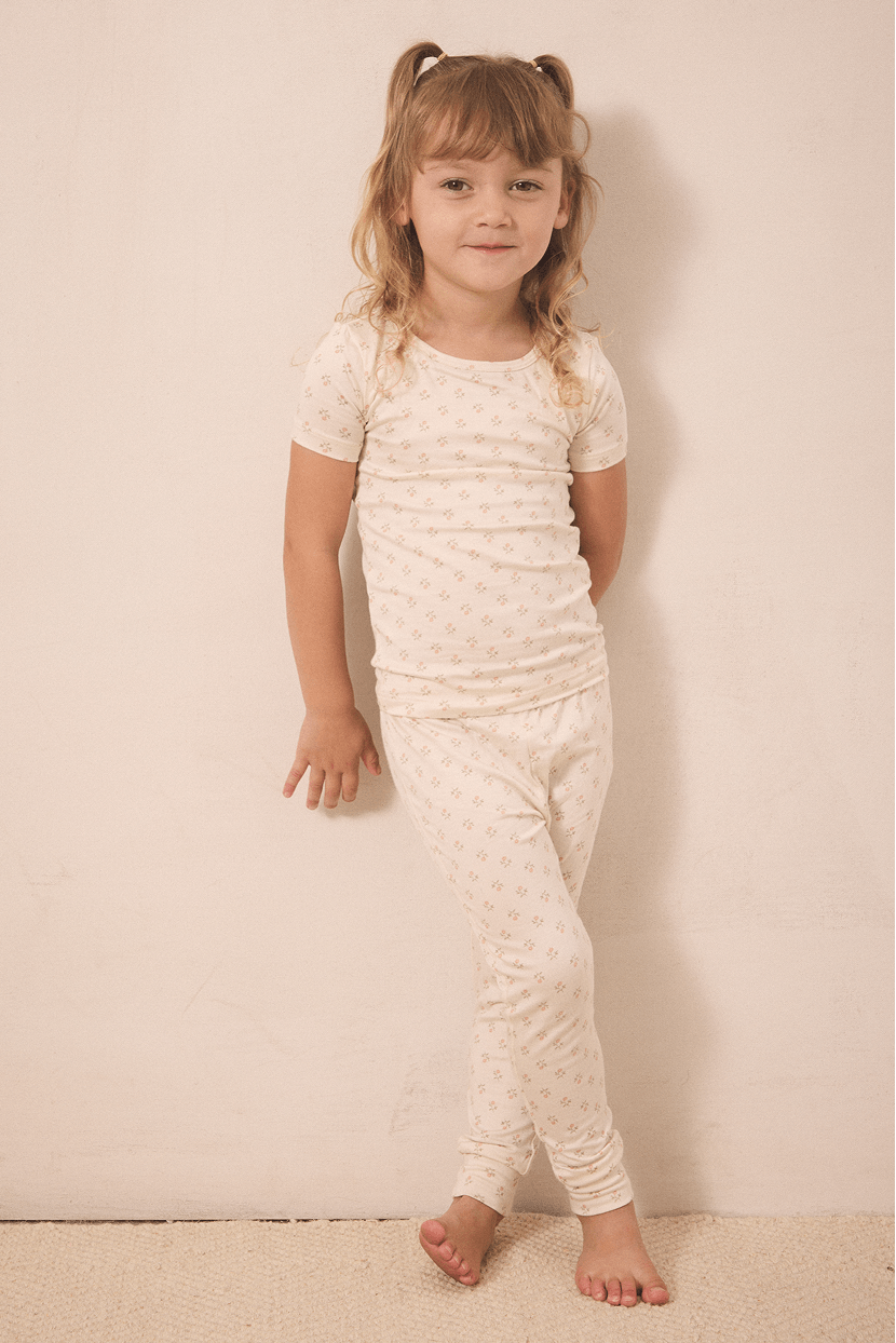 Girl wearing cream-colored short sleeve top and pants pajama set with small floral pattern.