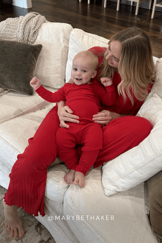 Woman and baby in red pointelle outfits sitting on a beige couch.