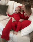 Woman and baby in red pointelle outfits sitting on a beige couch.