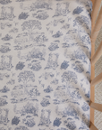 Beige chair cushion with detailed blue toile pattern featuring trees, animals, and countryside scenes.