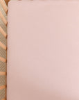 Light pink fitted crib sheet on a wooden crib mattress with beige carpet visible underneath.
