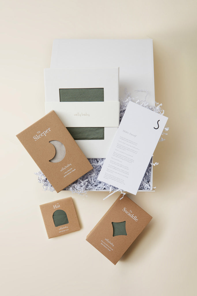 Gift box set with olive green baby sleeper, hat, and swaddle in kraft paper packaging, plus product information card.