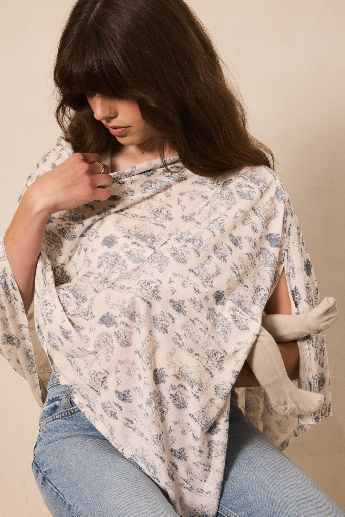 A woman wearing a cream-colored wrap top with a blue floral pattern and light blue jeans, posed against a neutral beige background.