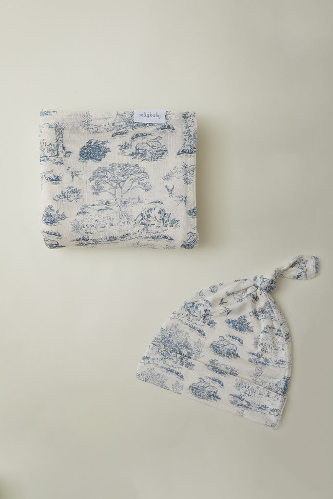 Cream-colored baby blanket and knotted hat set with blue nature and animal toile pattern