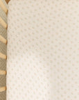 Crib mattress covered with white fitted sheet featuring small pink floral pattern inside light wooden crib.