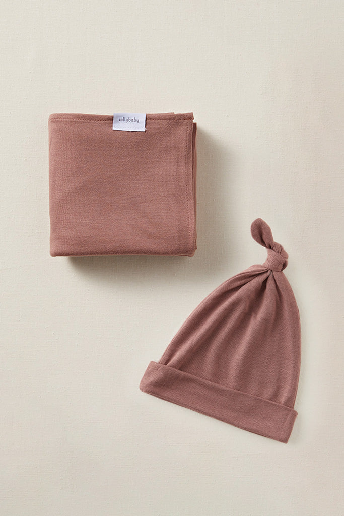 Dusty pink baby blanket with label and matching knotted baby hat on beige background.