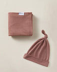Dusty pink baby blanket with label and matching knotted baby hat on beige background.