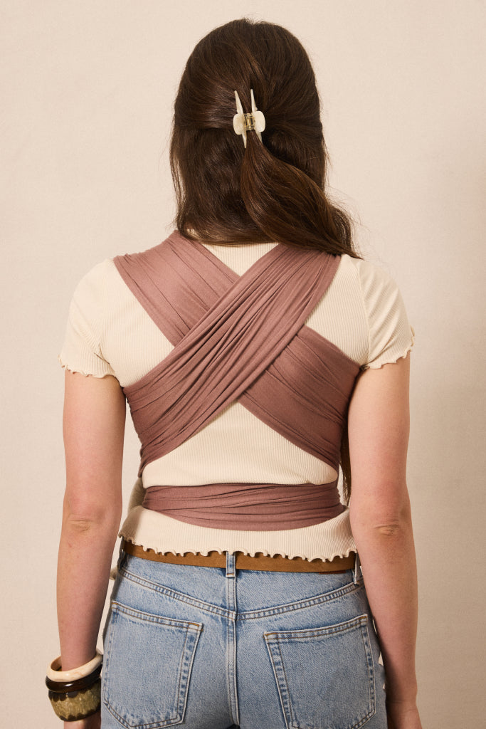 A woman viewed from behind wearing a mauve-brown crisscross back wrap top over a cream short-sleeve top, paired with light blue jeans.