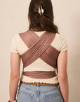 A woman viewed from behind wearing a mauve-brown crisscross back wrap top over a cream short-sleeve top, paired with light blue jeans.