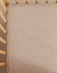 A close-up image of a Solly Baby Crib Sheet in the Cream Floral print featuring petite cream buds gently scattered atop a soft taupe brown base. 