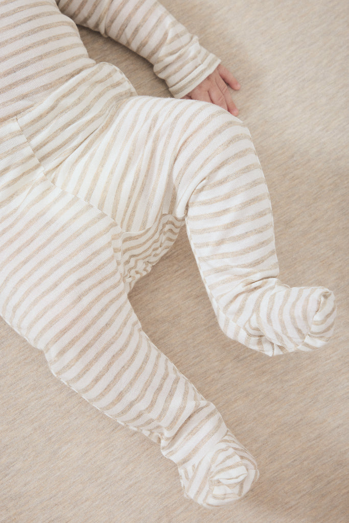 A close-up of a baby wearing cream and beige striped footed pajamas, lying on a soft beige blanket.