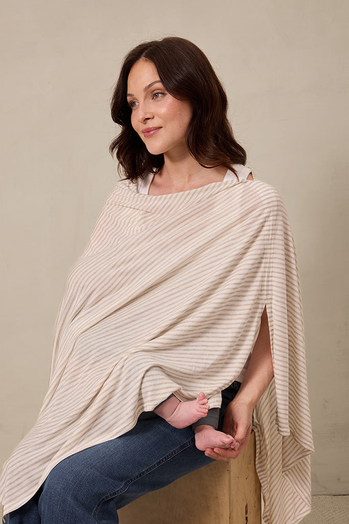 Beige and white striped nursing cover worn by woman sitting with baby feet visible underneath.