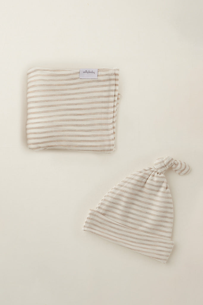 Beige and white striped baby blanket and knotted hat set on a cream background.