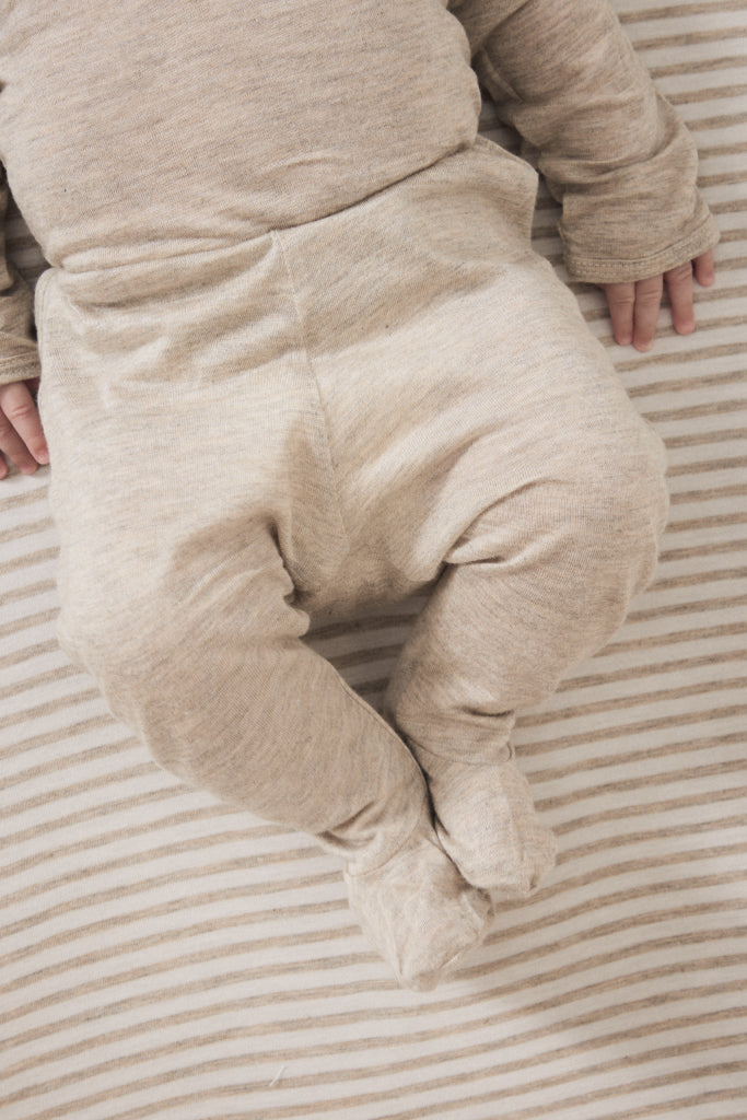 A close-up of a baby wearing a heathered beige footed sleeper, lying on a striped beige and white blanket.