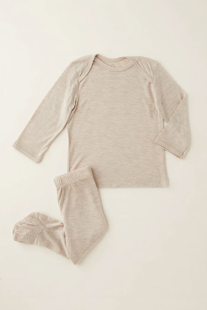 A two-piece baby pajama set in a heathered oatmeal beige color, featuring a long-sleeve top and matching footed pants, laid flat on a light cream background.