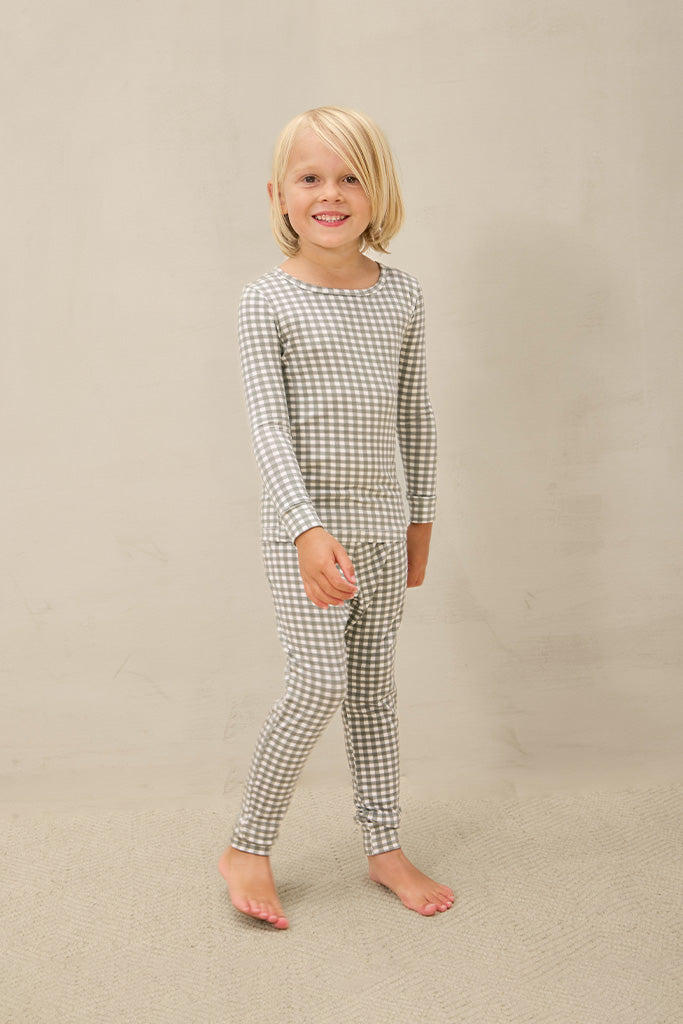 Child wearing gray and white gingham long-sleeve top and matching leggings pajamas standing barefoot.