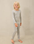 Child wearing gray and white gingham long-sleeve top and matching leggings pajamas standing barefoot.