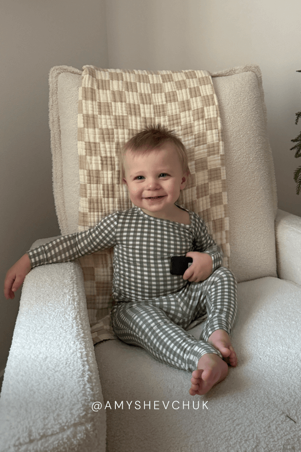 Child wearing a green and white gingham sleep set sitting on a cushioned chair with text overlay. Features the instagram handle @amyshevhuk