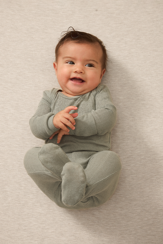 A baby wearing a mist pointelle sleep set on a beige background