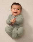 A baby wearing a mist pointelle sleep set on a beige background