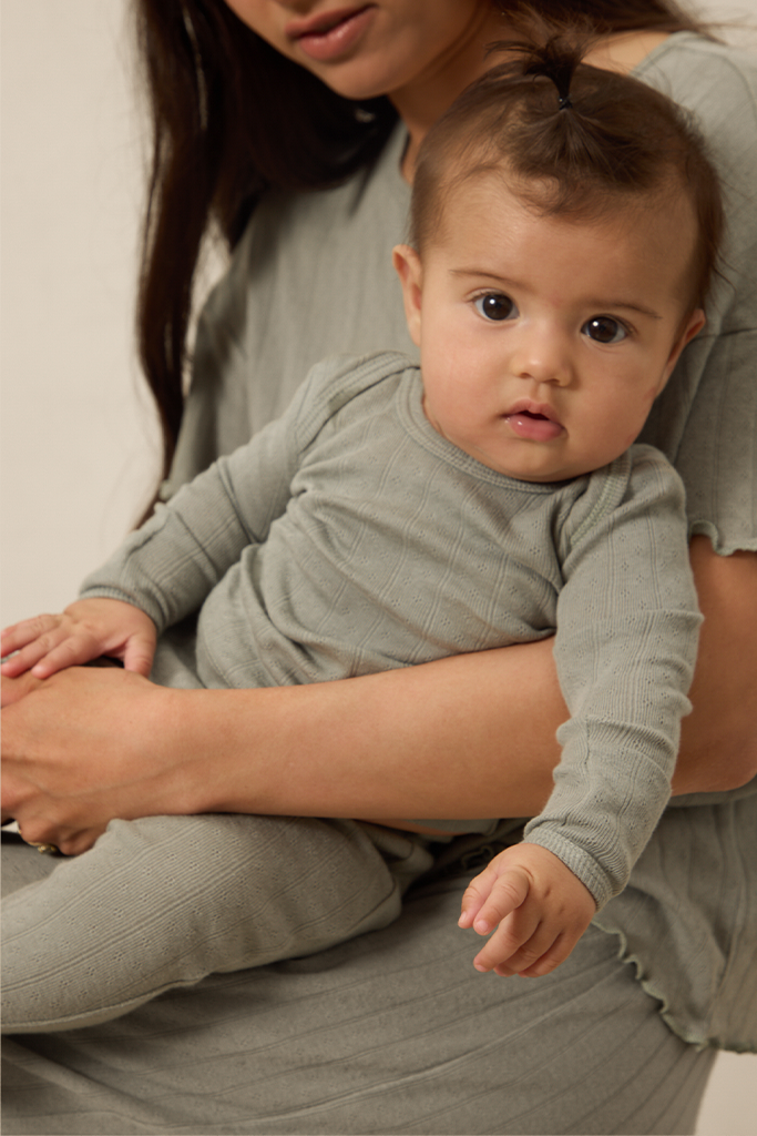 Baby sitting on a woman's lap wearing matching mist pointelle sleep sets