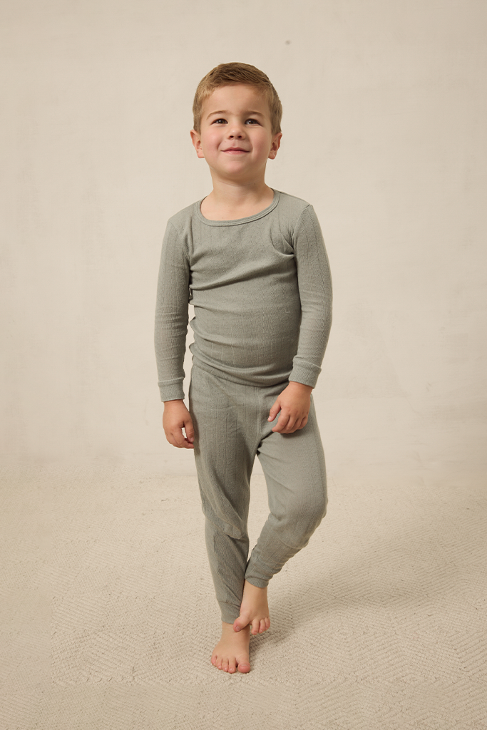 Young boy wearing a mist pointelle sleep set on a beige background