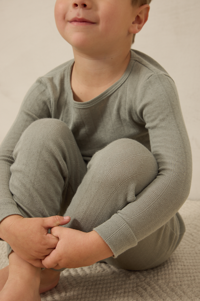 Child wearing a mist pointelle sleep set sitting on a beige surface.