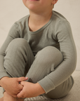 Child wearing a mist pointelle sleep set sitting on a beige surface.