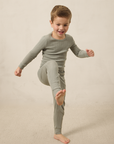 A boy wearing a mist pointelle sleep set, standing with one foot up on a neutral background