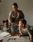 A woman holding a baby standing near two children sitting at a table with art supplies
