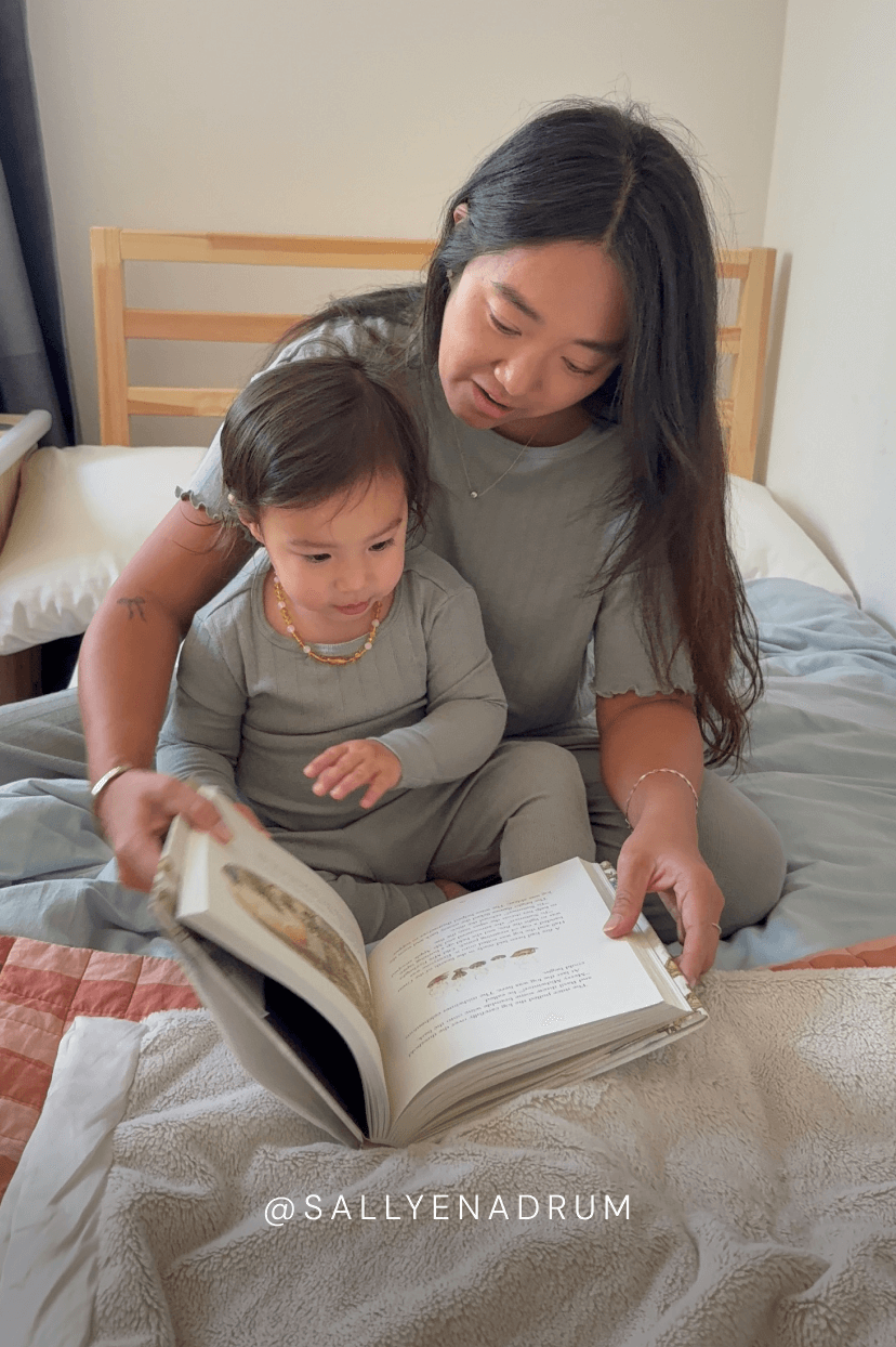 A woman and a child reading a book sitting on a bed in matching mist pointelle pajamas