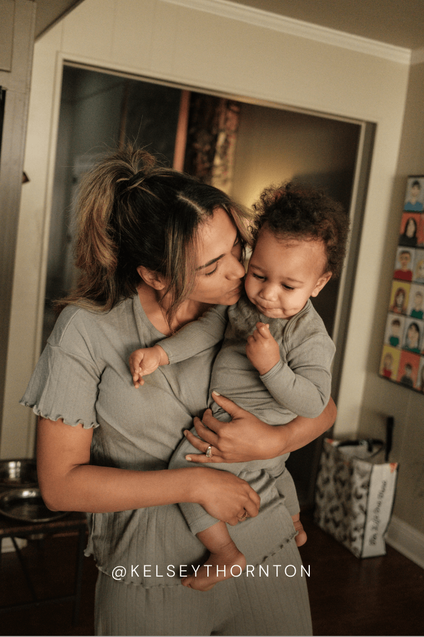Woman holding a baby in a home setting with decor in the background.