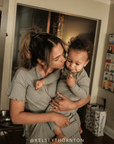 Woman holding a baby in a home setting with decor in the background.