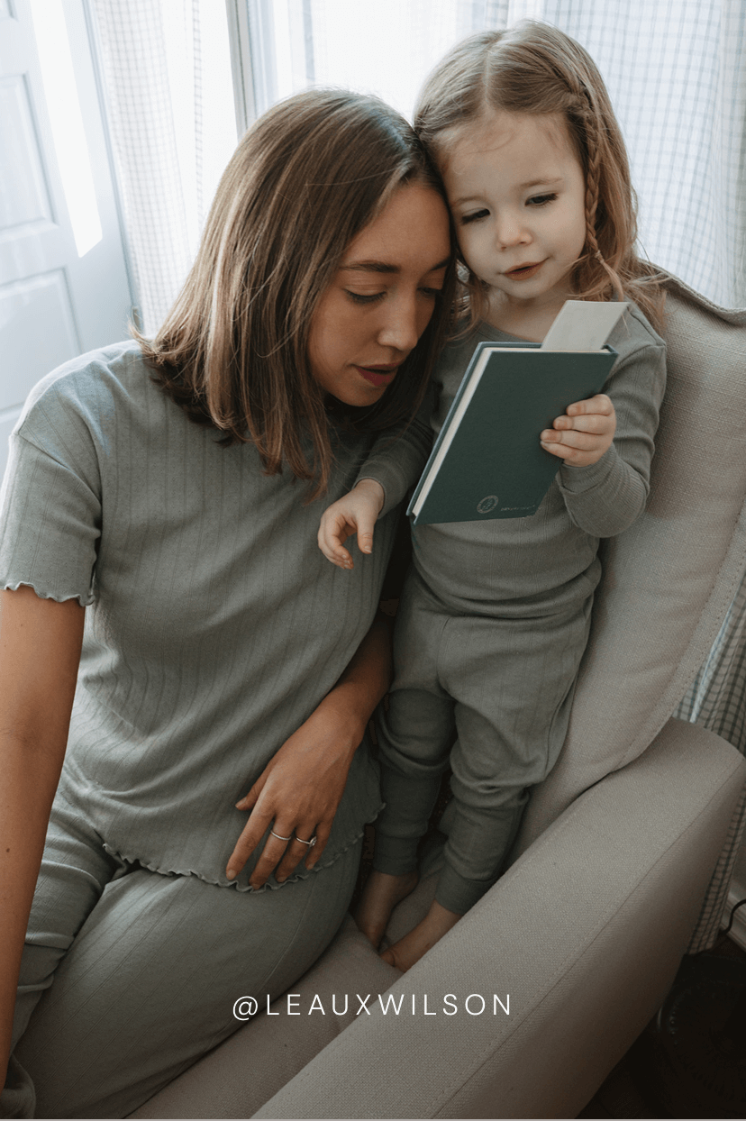 Woman and child sitting together on a chair, looking at a book.