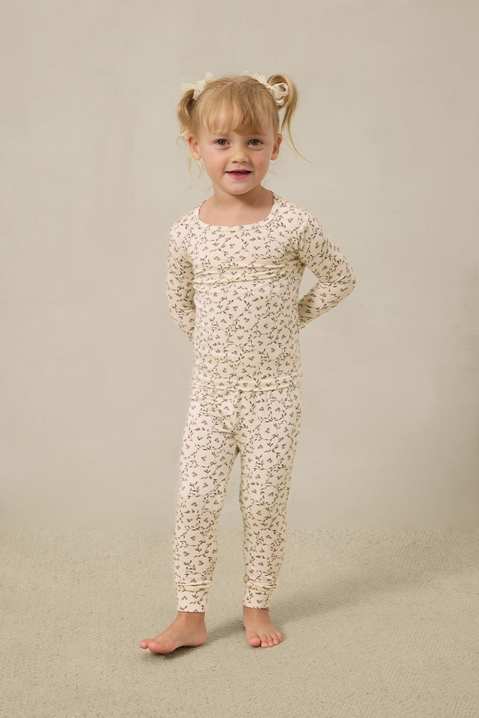 Toddler girl wearing cream-colored long-sleeve top and leggings with small brown floral print pajamas.