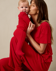 Woman in a red pointelle outfit holding a baby in red pointelle outfit against a beige background
