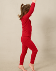 Child wearing a red pointelle outfit standing against a beige background