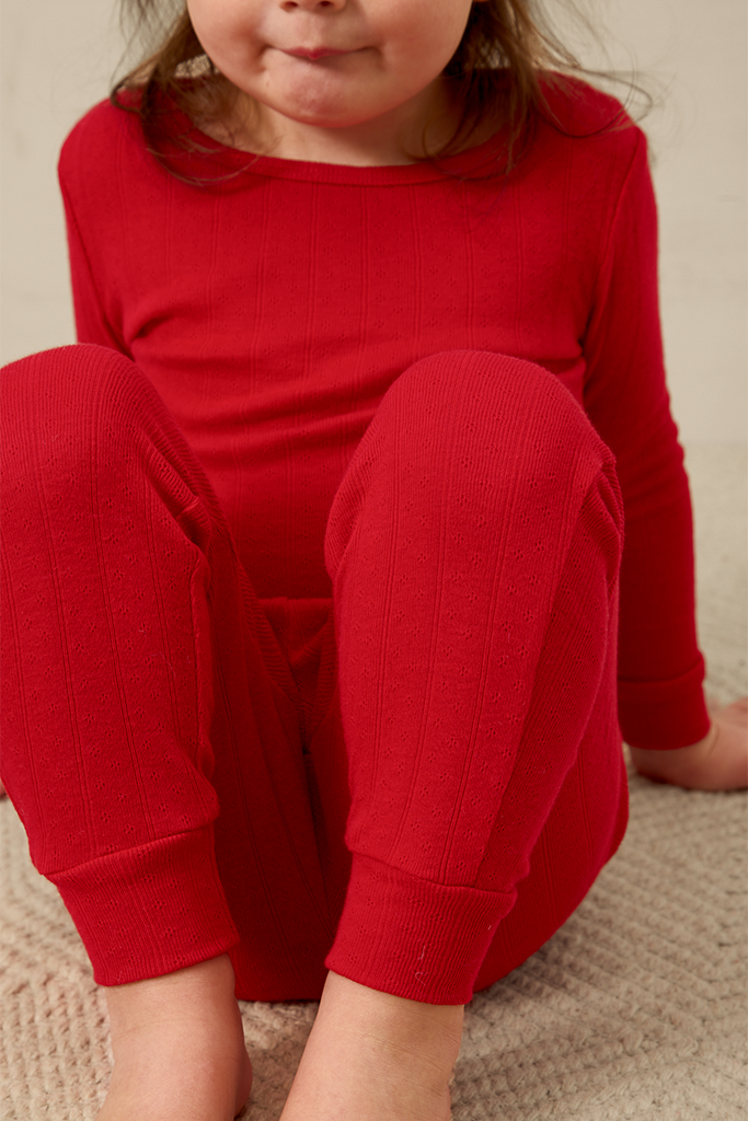 Child wearing a red pointelle outfit sitting on a beige surface