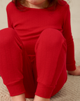 Child wearing a red pointelle outfit sitting on a beige surface
