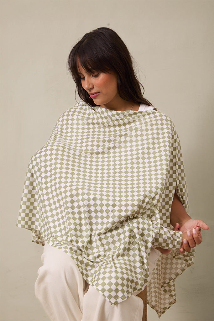 Woman wearing green and white checkered nursing cover with adjustable strap over white pants