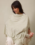 Woman wearing green and white checkered nursing cover with adjustable strap over white pants