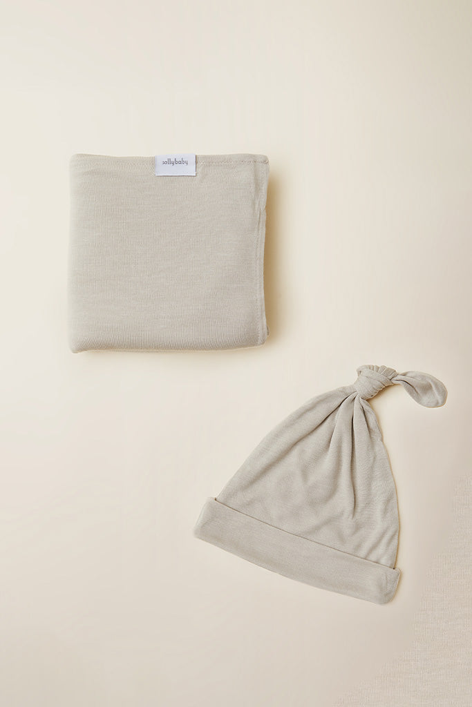 Beige baby blanket with label and matching beige baby knotted hat on light background.