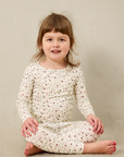 Young girl wearing a strawberry pajama set sitting on a beige floor.