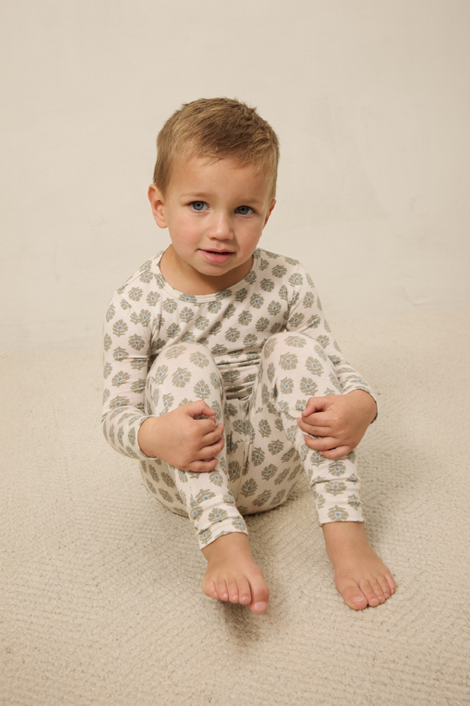 Child wearing a patterned onesie sitting on a beige surface