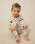 Child wearing a patterned onesie sitting on a beige surface