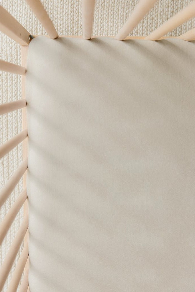 Beige fitted crib sheet on natural wood crib with textured cream rug underneath.