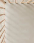 Beige fitted crib sheet on natural wood crib with textured cream rug underneath.